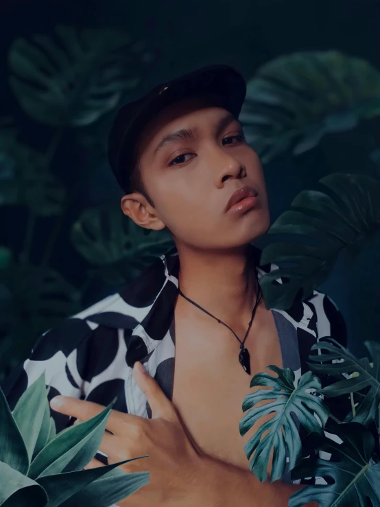 a man with black and white shirt, hat and green leaves in front of him