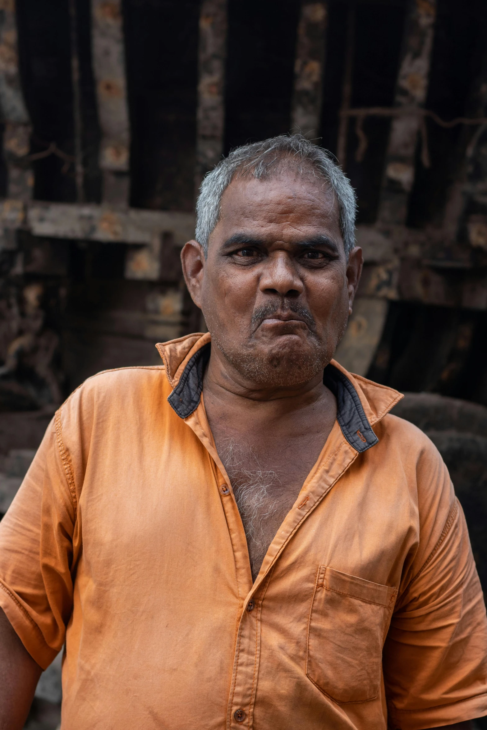 a man with grey hair and orange shirt stands in front of an unlit wooden structure