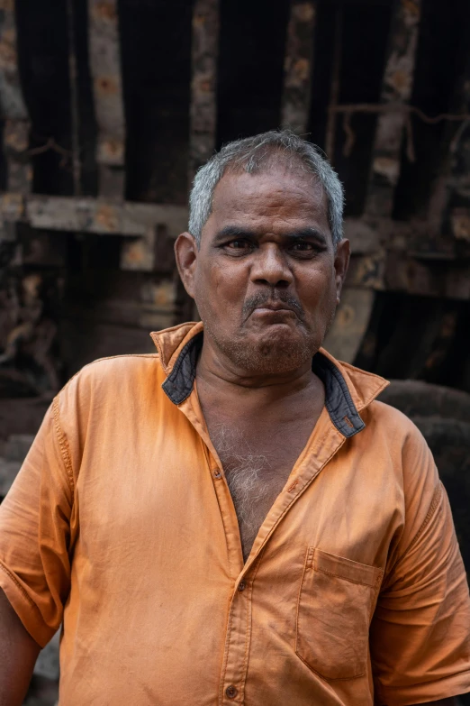 a man with grey hair and orange shirt stands in front of an unlit wooden structure