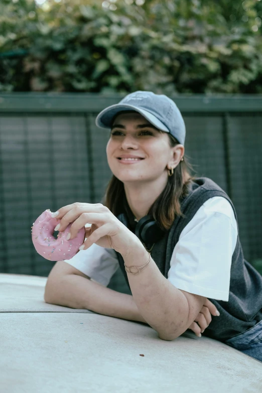 a smiling woman sitting on the ledge eating a donut