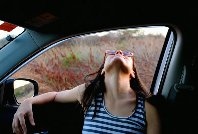 a woman sitting in the back seat of a car with her head out of a window and eyes wide open