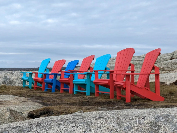 a bunch of red, blue and green chairs sitting on some rocks