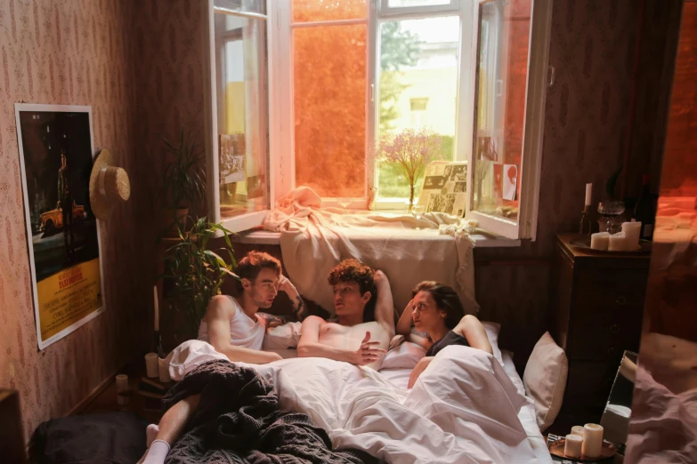 four people laying in a bed in a bedroom with windows