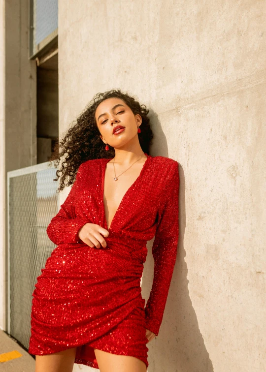 the woman wearing a red dress poses against a concrete wall