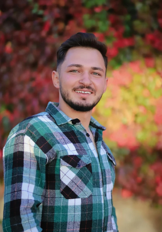 a man smiles while standing in front of an autumn tree