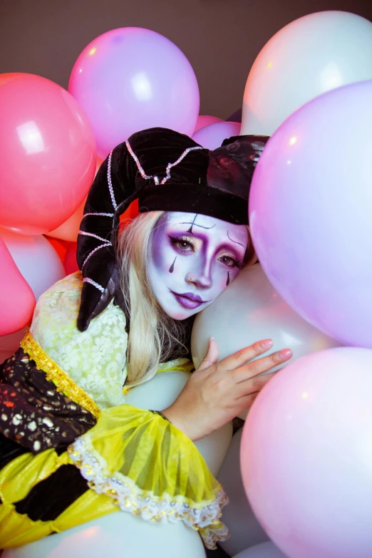 a lady with her face painted as a bee sits among balloons