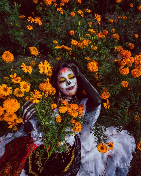 a woman with face painted sitting on grass holding flowers