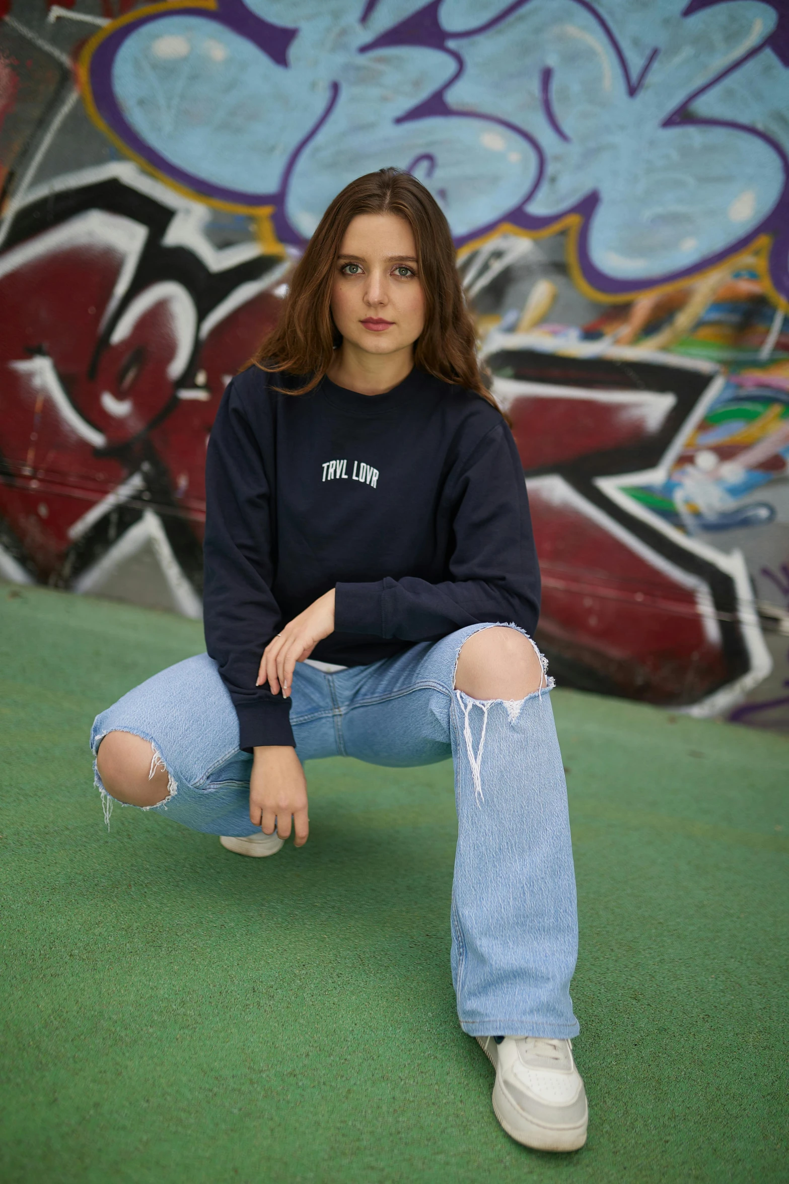 a girl sitting down in front of a graffiti wall