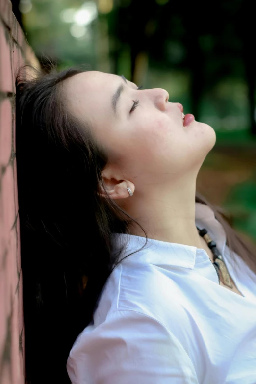 a woman in white shirt standing against wall next to brick wall