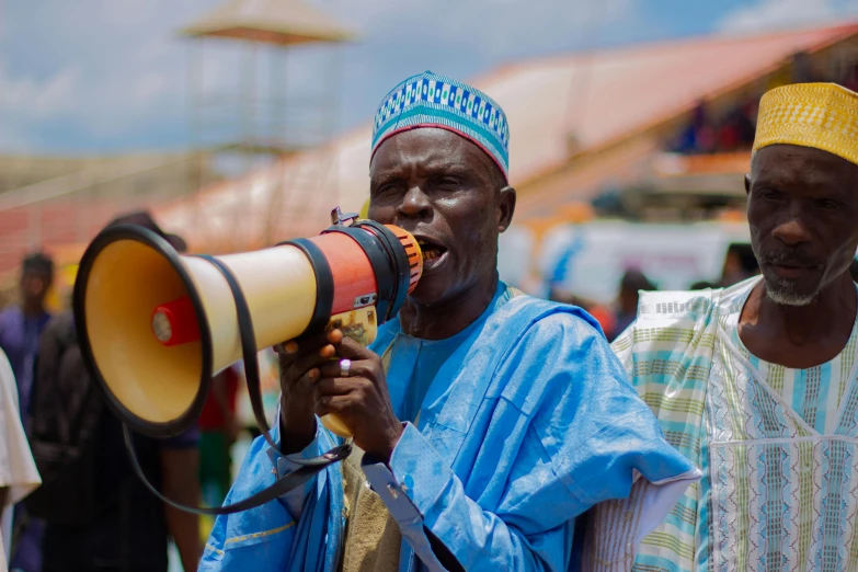 two men speaking through a small yellow and red megaphone