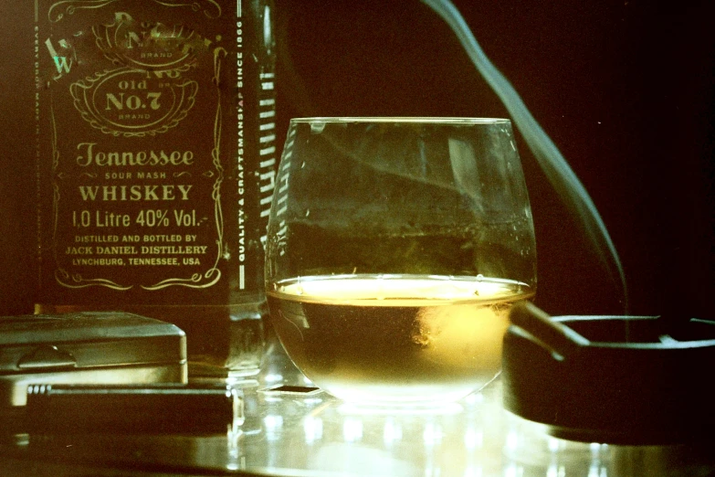 a glass on a table next to a bottle of liquor