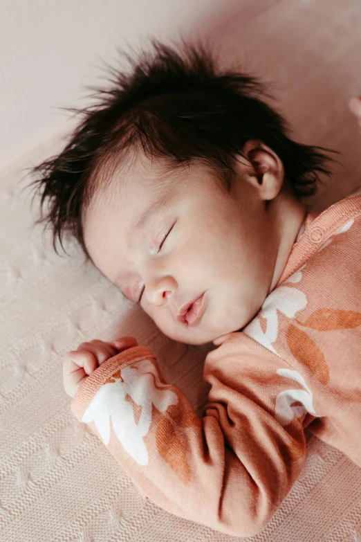 a baby sleeping on its back while wearing an orange and white sweater