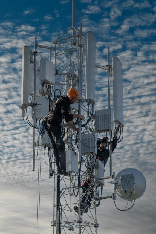 two men working on a phone tower with blue sky in the background