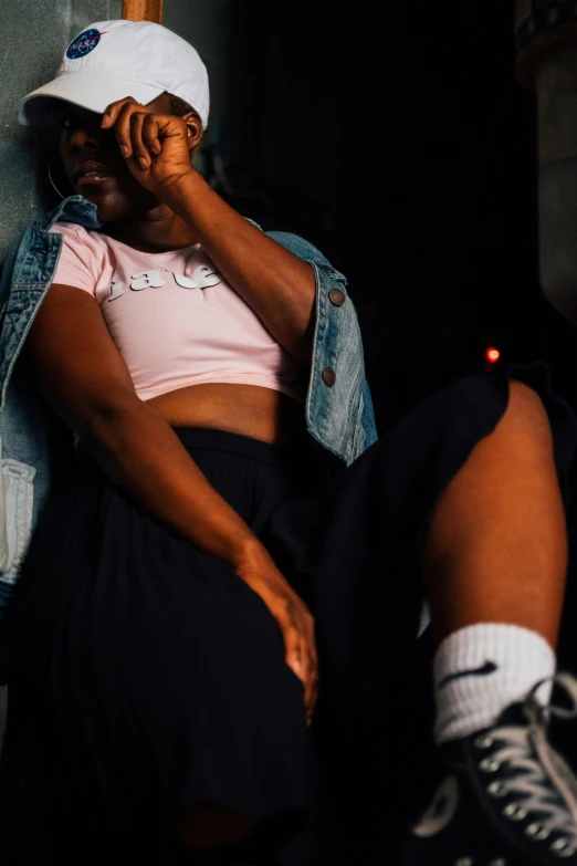 a girl sitting in the shadows wearing a cap and a pink shirt