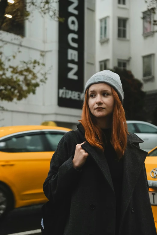 a woman in black coat standing on street next to taxi