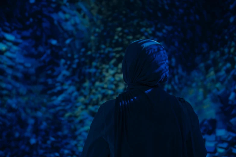 a person in black wearing a hood is looking down at an abstract background