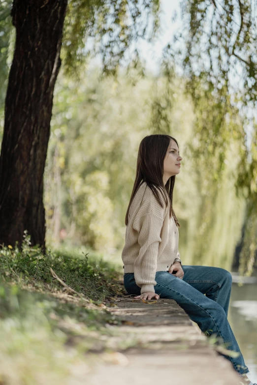 a girl sitting down on a sidewalk, near the river