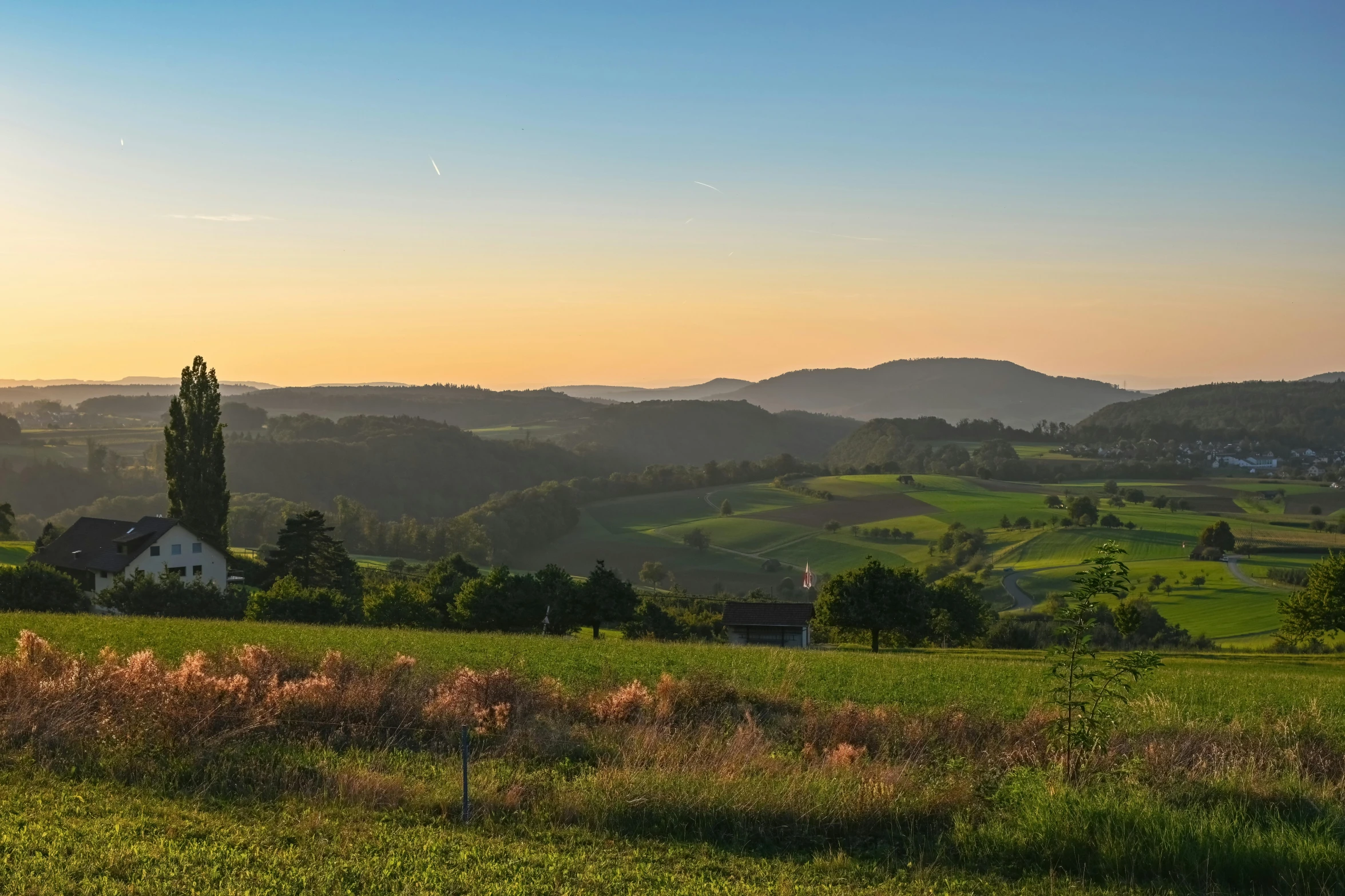 the sun sets over the rolling hills in a rural area