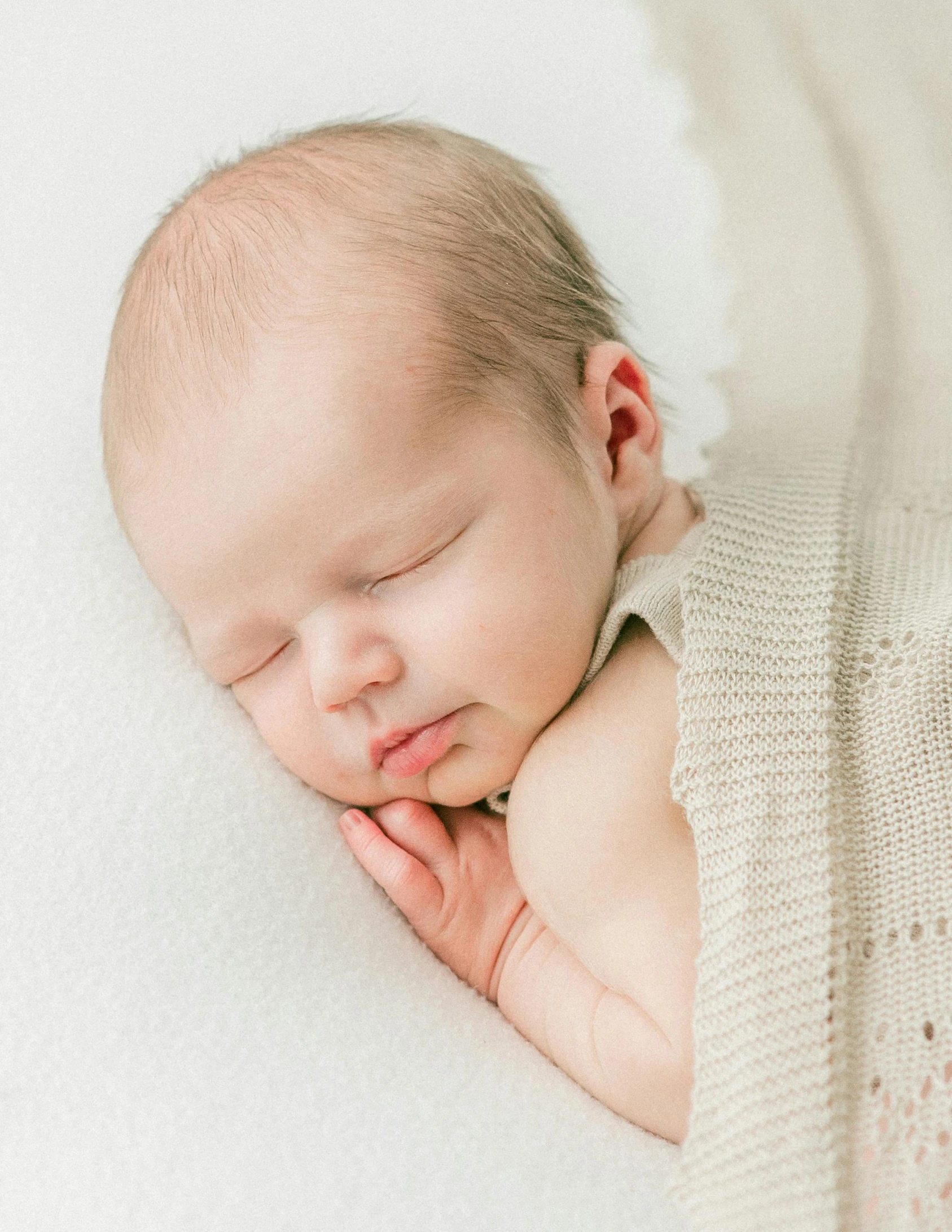 a sleeping baby is posed in a white outfit