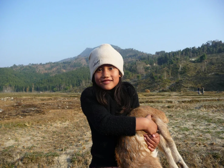 a girl in a knit hat holding a little goat