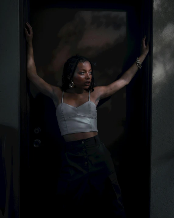 a young woman poses in the shadows while leaning against an open doorway