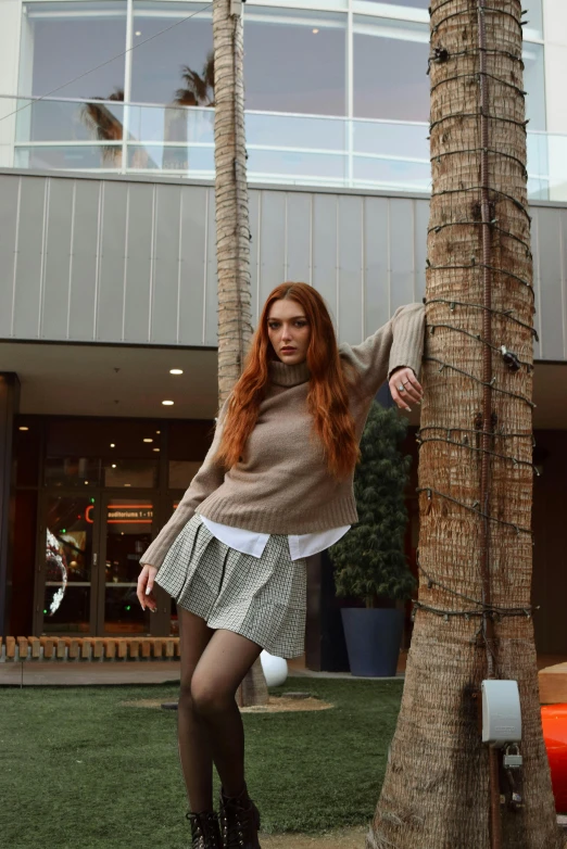 a woman with red hair wearing boots standing next to a palm tree