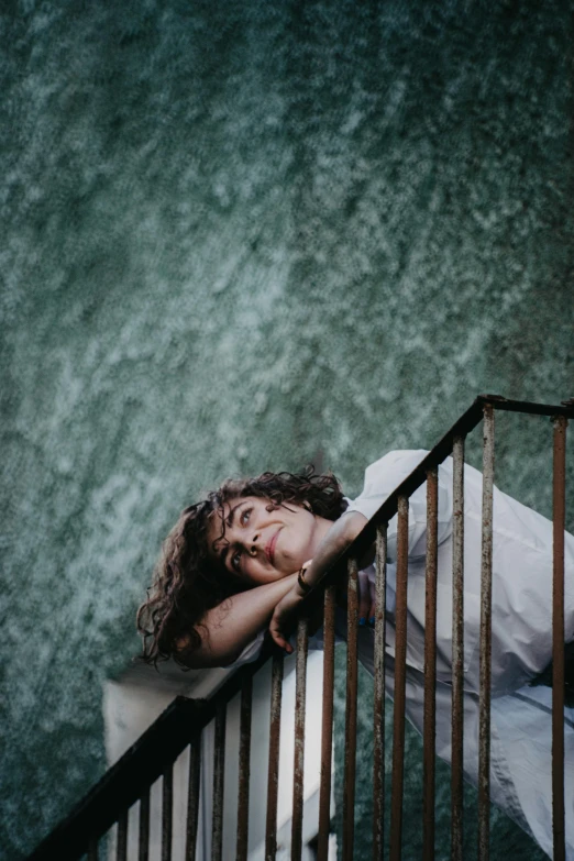 a woman with long hair leaning on a railing, in front of green water