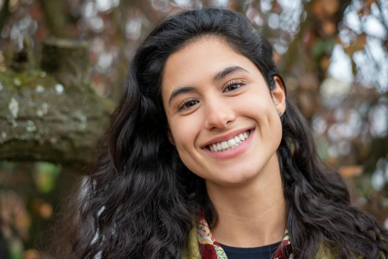 a woman smiling for the camera with a tree in the background