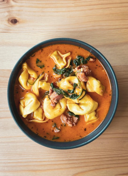 a black bowl filled with tortelli soup