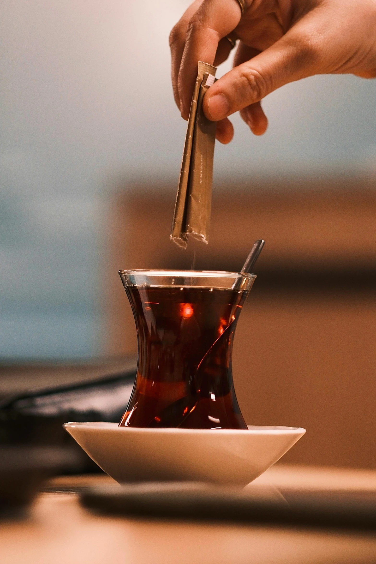 a hand holding a piece of paper with a spoon over a teacup filled with tea