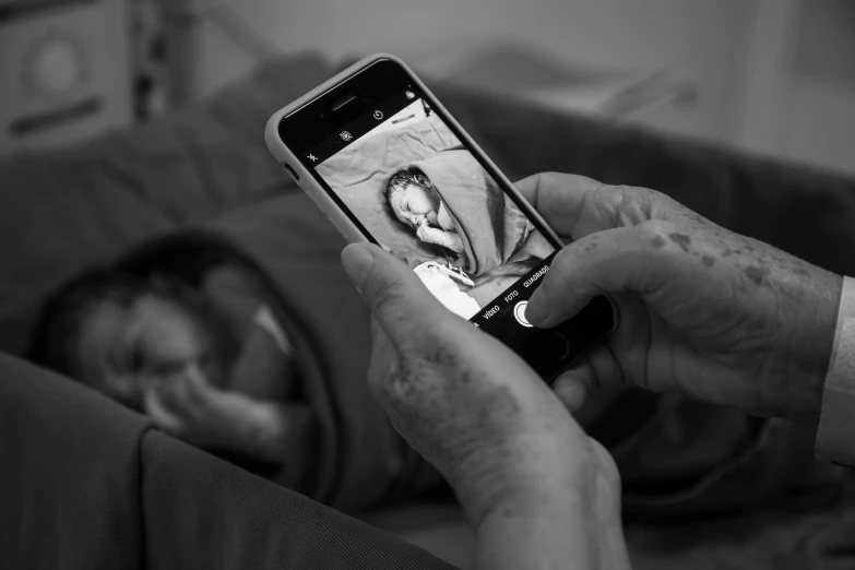 a hand holds a smart phone over a baby in a crib