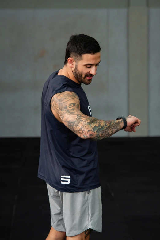 a man with tattoos on his arm is standing in front of a concrete wall