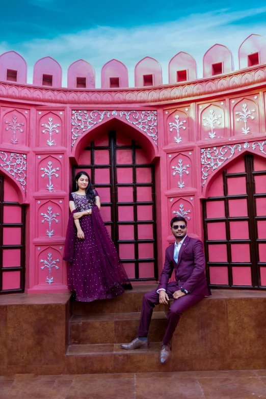 a man and woman are posed for a picture in front of a pink building
