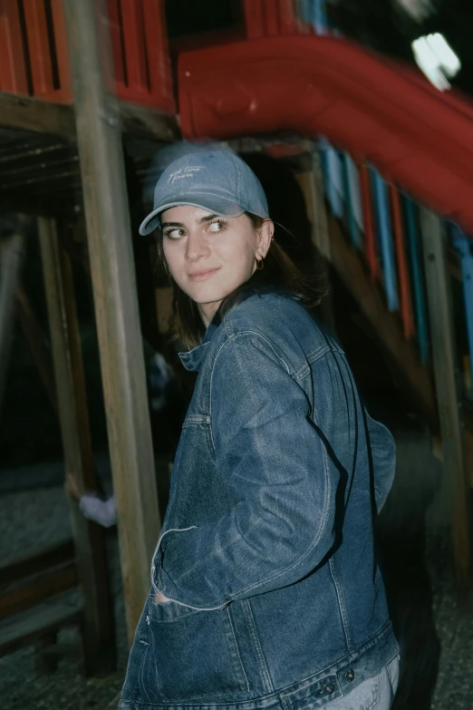 young woman in denim jacket and cap on skateboard in front of building