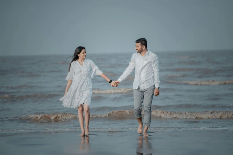 a man and a woman holding hands walking along the ocean shore