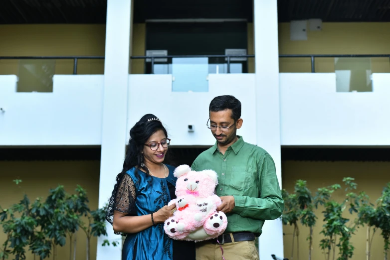 a man and woman holding two teddy bears while standing next to each other