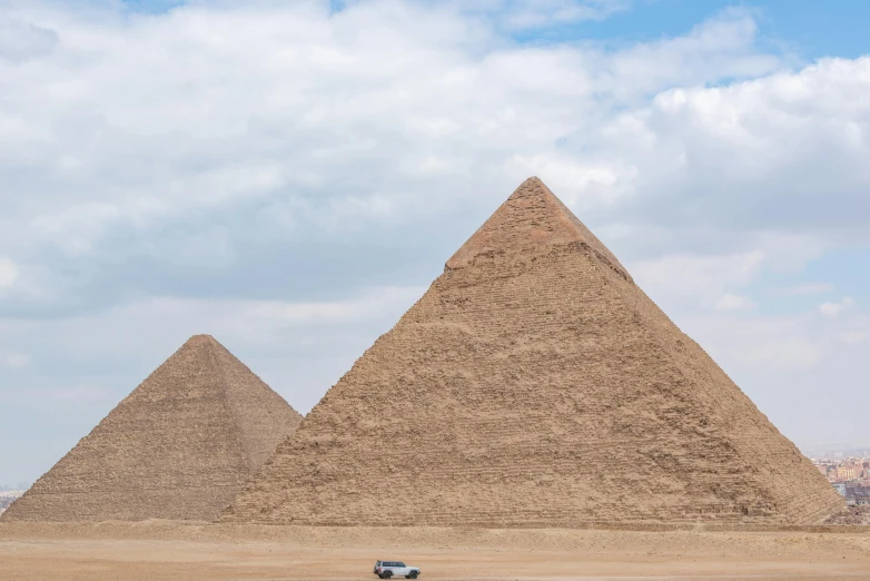 a truck drives next to three pyramids in the desert