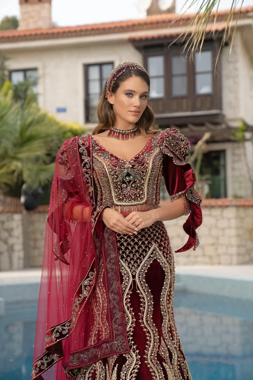 a model wearing an ornate burgundy gown and red veil, and carrying a fan