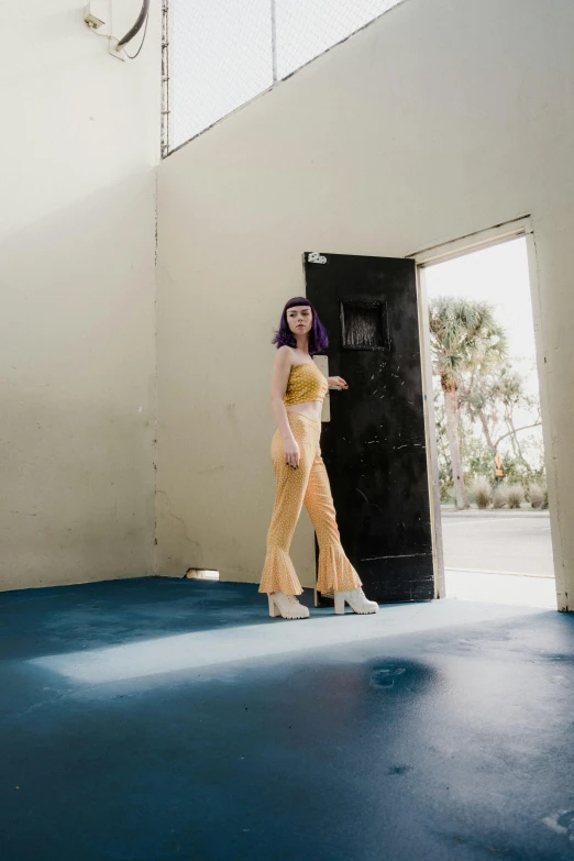 a model with long purple hair stands on the floor wearing yellow