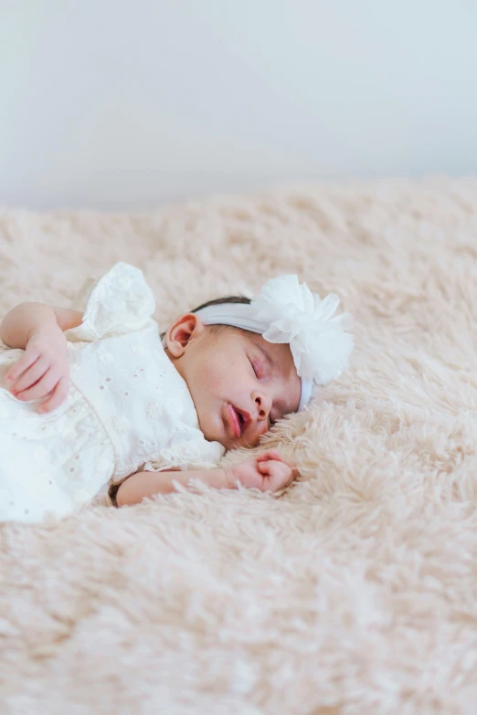 a newborn baby wearing a white dress and bow is asleep