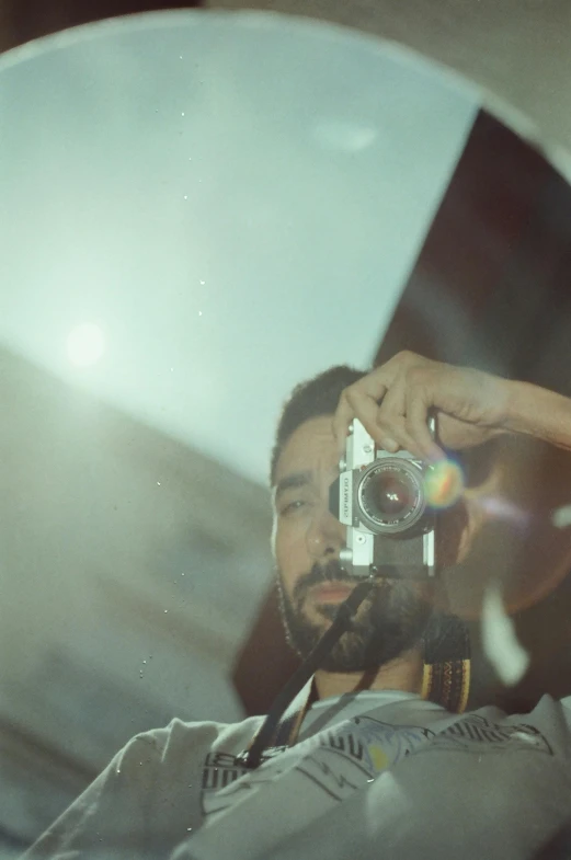 man with beard is holding a camera and taking a picture in the mirror