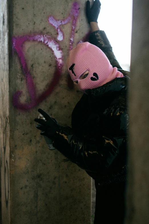 a woman with pink hat and black coat reaching up at graffiti on wall