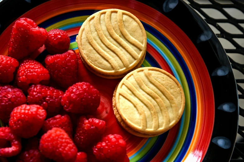 a colorful plate with cookies, raspberries and other food