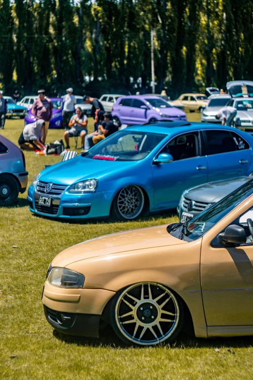 several parked cars in a field with people sitting on benches