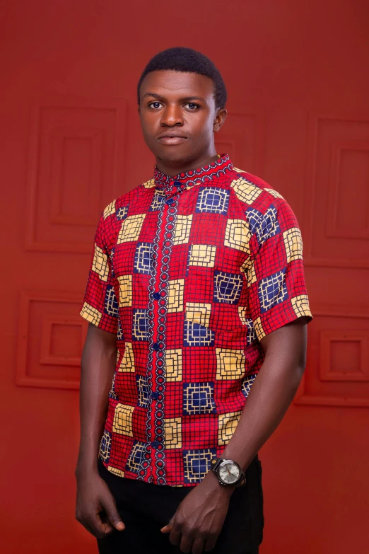 a man in a red and yellow patterned shirt poses in front of a red wall