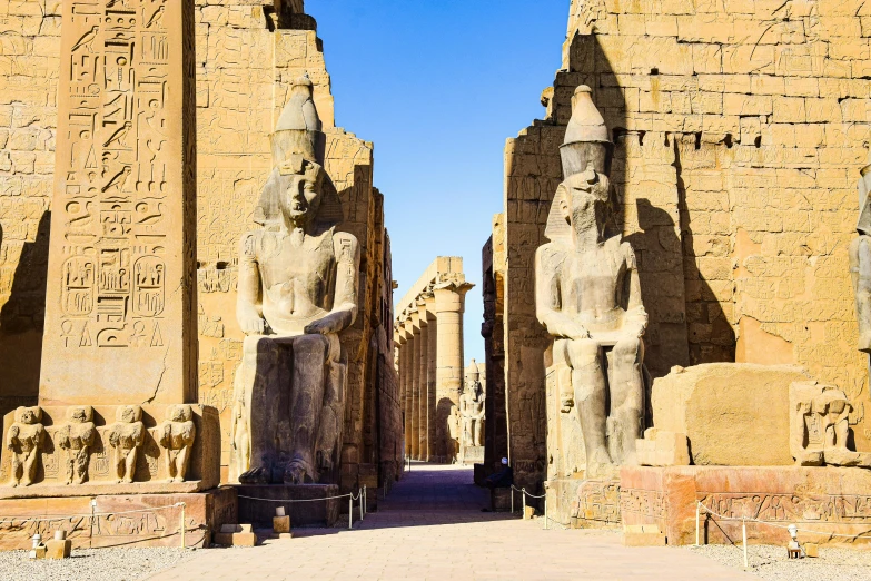 two statues in front of egyptian buildings with one sitting on a bench