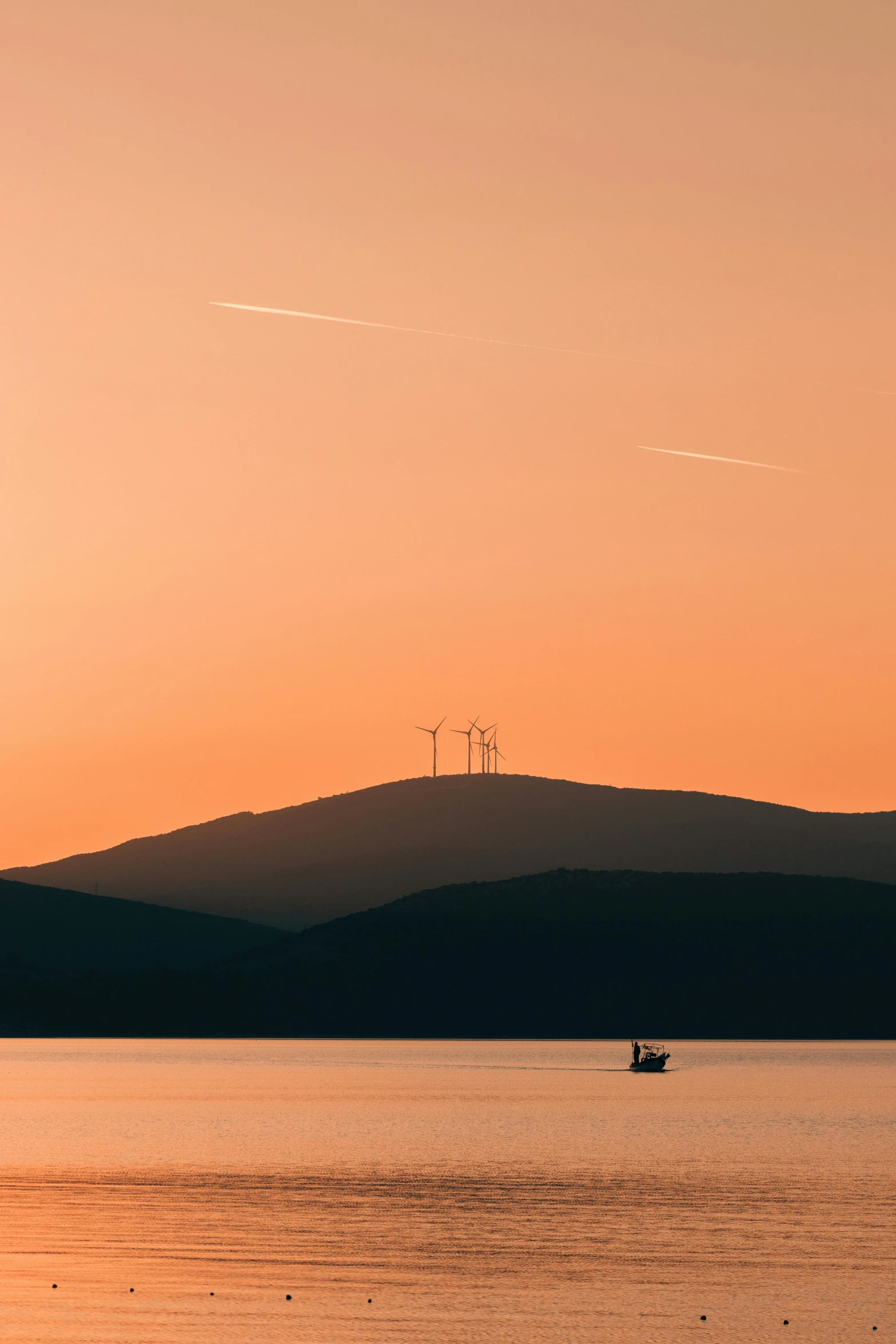 sunset po of wind generators on a hill over water