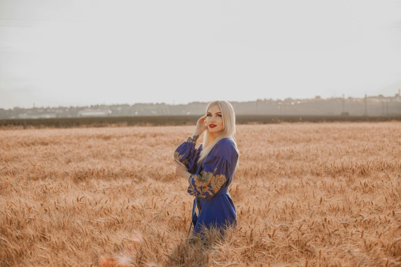 a beautiful blonde woman standing in a field of wheat