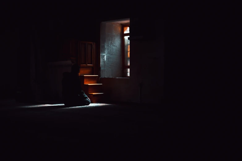 a person sits in the dark looking through an open door