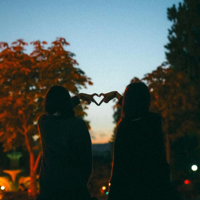 two women are holding their hands to form a heart shape